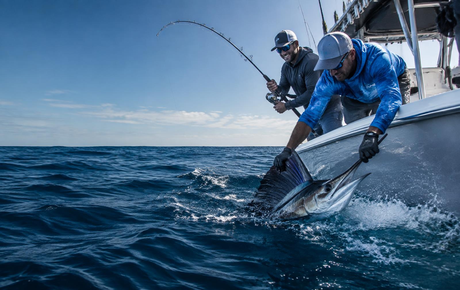 A guide helps a guest land a marlin beside a sport fishing boat